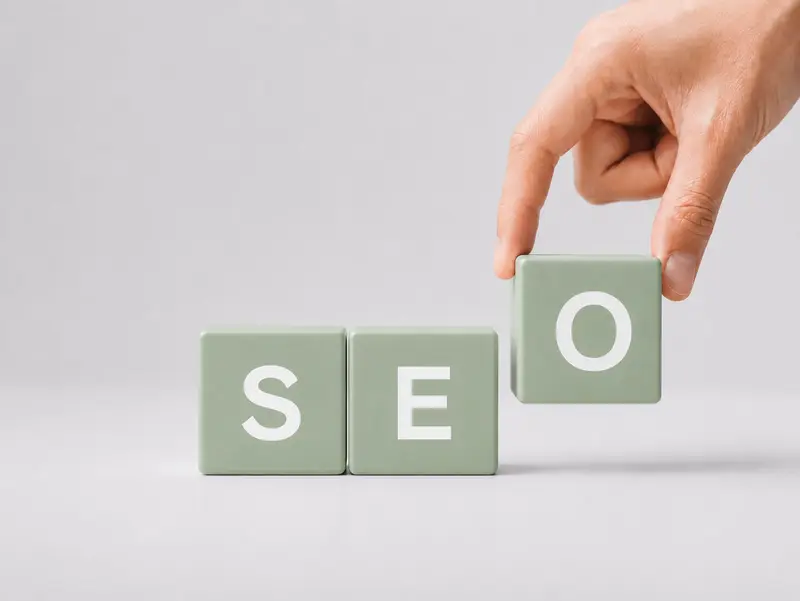 Grüne Buchstabenwürfel bilden das Wort SEO – eine Hand setzt den letzten Baustein.