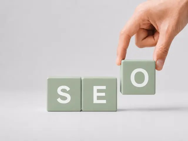 Grüne Buchstabenwürfel bilden das Wort SEO – eine Hand setzt den letzten Baustein.